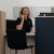 A friendly receptionist with wavy blonde hair sits at a modern desk, smiling as she answers a corded phone in a reception area.