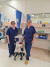 Two friendly medical professionals in navy scrubs stand beside a monitor in a bright, well-equipped private hospital room.