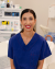 A female healthcare professional in blue scrubs smiles calmly in a well-equipped, clean clinical environment.