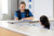 A friendly staff member in a blue uniform completes paperwork at a reception desk, communicating with a colleague in a hospital setting.