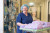 A healthcare professional in blue scrubs and hair net transports sterilized medical supplies on a cart in a clean hospital corridor.