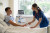 A nurse in blue scrubs attentively checks the pulse of a young male patient in a hospital bed, with modern equipment nearby and sunlight shining through large windows.