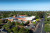 Aerial view of a private hospital in a suburban area with ample parking, tree-lined streets, and a distant city skyline under clear skies.