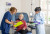 Two healthcare professionals support an older woman in a medical chair, providing care and information in a well-equipped setting.