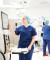 A healthcare professional in blue scrubs uses advanced touchscreen equipment in a bright, modern hospital room, with another staff member nearby.