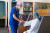 A healthcare professional in scrubs helps a seated patient in a private hospital waiting area, ensuring comfort and attentive care.