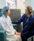 A healthcare professional provides support to a patient in a bathrobe and hair cover in a private hospital waiting area.