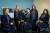 Five staff members in matching uniforms smile in a well-equipped office with blue and beige walls and visible computer workstations.