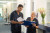 Two healthcare professionals in black scrubs review documents together in a hospital hallway. Flowers in a vase are on the counter nearby.
